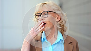 Mature blonde businesswoman in glasses yawns from boredom