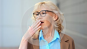 Mature blonde businesswoman in glasses yawns from boredom