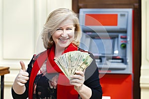 Mature blonde woman counting money near ATM