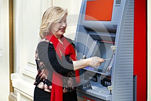 Mature blonde woman with credit card in hand near ATM