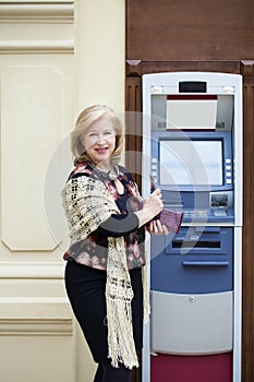 Mature blonde woman with credit card in hand near ATM