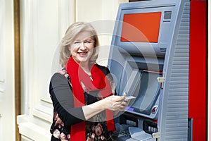 Mature blonde woman with credit card in hand near ATM