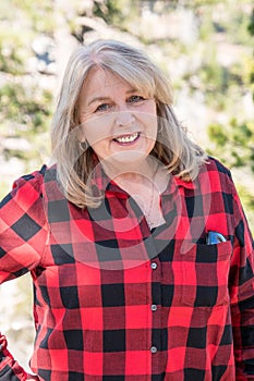 A mature blonde woman wearing a buffalo plaid flannel shirt red and black poses for a portrait in the Eastern Sierra Nevada