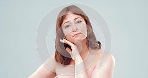 Mature brown-haired female applies skin care cream by touching face with hand, close up. Woman applying anti-age cream