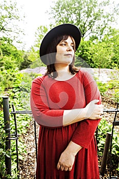 mature brunette woman in green garden wearing hat, smiling, frie