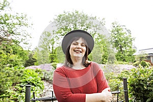 Mature brunette woman in green garden wearing hat, smiling, friendly welkoming, lifestyle people concept close up