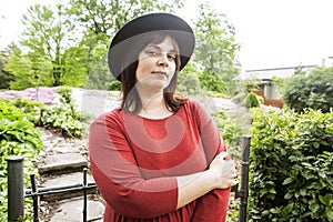 Mature brunette woman in green garden wearing hat, smiling, friendly welkoming, lifestyle people concept close up