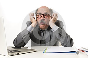 Mature business man with bald head on his 60s working stressed and frustrated at office computer laptop desk looking desperate