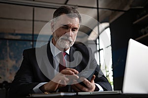 Mature business man in formal clothing using mobile phone. Serious businessman using smartphone and laptop at work