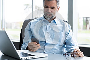 Mature business man in formal clothing using mobile phone. Serious businessman using smartphone at work. Manager in suit