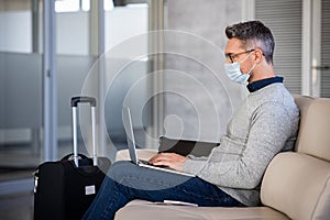 Mature business man wearing mask while commuting and using laptop