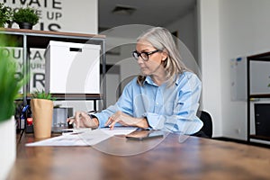 mature business woman in a blue shirt works at a table in the office