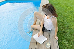 Mature business woman, freelancer, blogger with computer laptop and glass of water near the pool