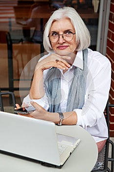 Mature business woman sets at table with laptop in small cafe business, exuding professionalism and entrepreneurial