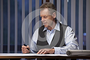 Mature businessman, architect or engineer  working at home at a desk late at night