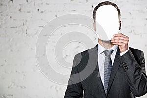 Mature businessman covering face with blank paper against white brick wall at office
