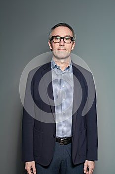 Mature businessman in dark blue suit and checked shirt on grey wall background