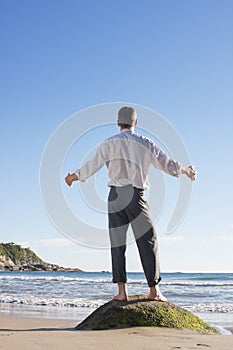 Mature businessman enjoying the sun while standing on a rock