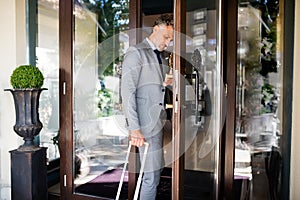 Mature businessman entering hotel with luggage.