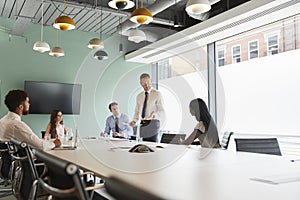 Mature Businessman Giving Boardroom Presentation To Colleagues In Meeting Room