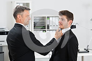 Mature Businessman Gripping Employee's Tie photo