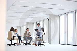 Mature businessman having discussion with team on chair in new office