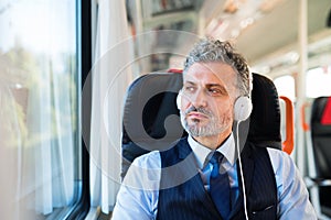 Mature businessman with headphones travelling by train.