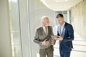 Mature businessman and his young colleague discussing finantial report on digital tablet in the office corridor