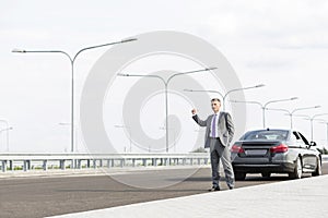 Mature businessman hitchhiking while standing with breakdown car on road