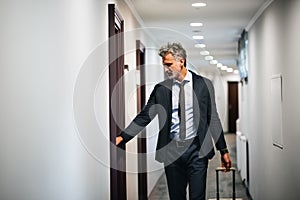 Mature businessman with luggage in a hotel corridor.