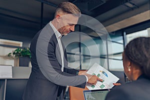 Mature businessman manager is holding documents consulting client at office meeting