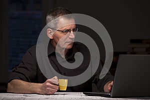 Mature businessman or manager working at home with laptop and a cup of espresso in his hand