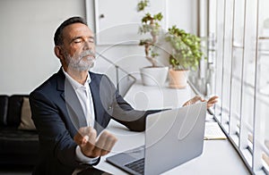 Mature Businessman Meditating With Eyes Closed At Laptop In Office