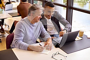 Mature Businessman Mentoring Younger Colleague Working On Laptop At Desk