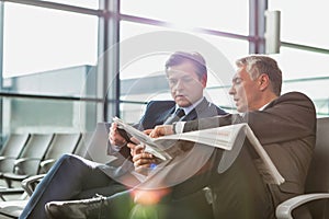 Mature businessman reading news paper while the other businessman is talking on smartphone in airport