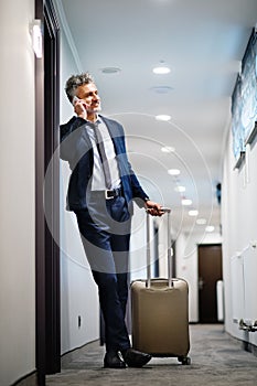 Mature businessman with smartphone in a hotel corridor.