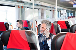 Mature businessman with smartphone travelling by train.