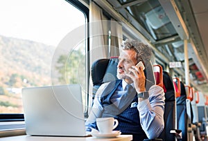 Mature businessman with smartphone travelling by train.