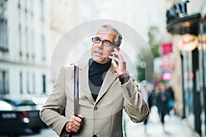 Mature businessman standing on a street in city, using smartphone.