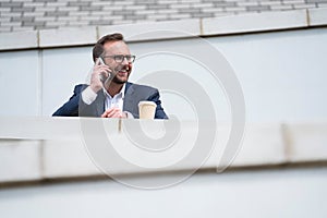 Mature Businessman Taking Phone Call On Mobile Phone Standing Outside Office Building