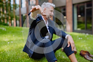 Mature businessman throwing away his smarthpone when sitting barefoot in park, feeling free, escaping from work concept.