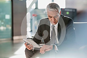 Mature businessman using digital tablet while checking time on his watch in airport