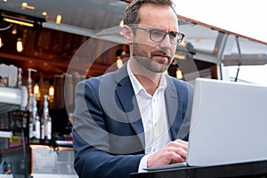 Mature Businessman Working On Laptop By Outdoor Coffee Shop