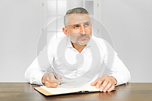 Mature businessman writing at desk in office. He works hard, from home or the office