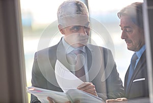 Mature businessmen discussing over document seen through glass in new office