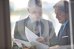 Mature businessmen discussing over document seen through glass in new office
