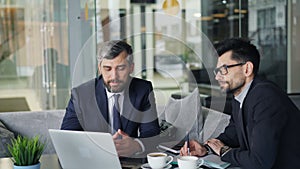 Mature businessmen talking in cafe looking at laptop screen discussing contract