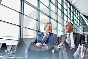 Mature businessmen talking while sitting and waiting for boarding in airport