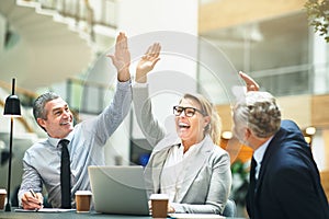 Mature businesspeople cheering and high fiving together in an of