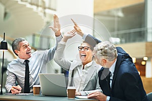 Mature businesspeople excitedly high fiving together in an offic photo
